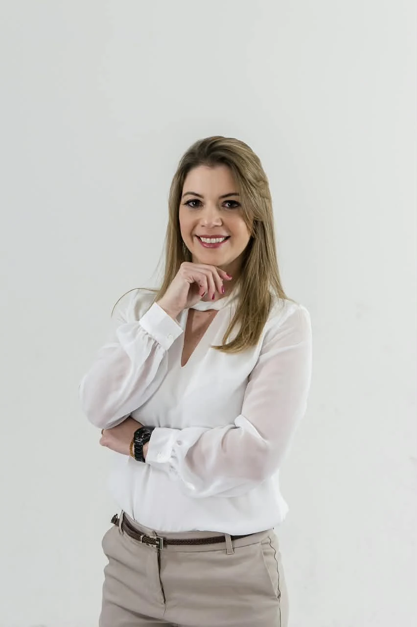 Adriana Decelli de blusa branca, com a mão no queixo, sorrindo